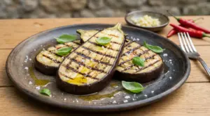 Fette di melanzane grigliate su un piatto con olio, sale e foglie di basilico