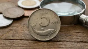 Moneta da 5 lire del 1956 con delfino in primo piano su sfondo di altre monete e lente d'ingrandimento