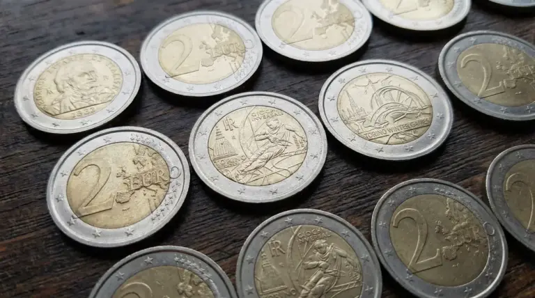 Vari esemplari di monete da due euro, alcune coni commemorativi su un tavolo in legno.
