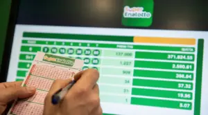 Una persona compila una schedina del SuperEnalotto davanti a uno schermo con i risultati.