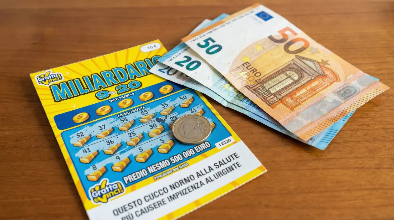 Biglietto Gratta e Vinci su un tavolo con banconote in euro e una moneta, legate a una possibile vincita tassata