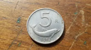 Moneta da 5 lire del 1954 con delfino, fotografata su un tavolo di legno