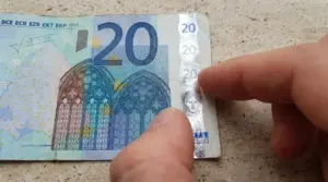 Primo piano di una banconota da 20 euro con dita che indicano la striscia olografica di sicurezza