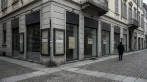 Vetrine di negozi vuoti con serrande abbassate in una via del centro, mentre una persona cammina sul marciapiede